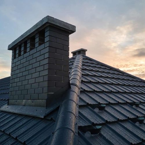Chimney on house roof top covered with metallic shingles under construction.