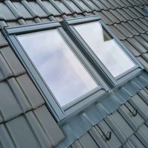 Closeup of attic window on house roof top covered with ceramic shingles. Tiled covering of building