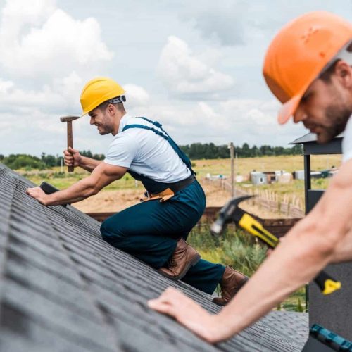 selective focus of handsome handyman repairing roof with colleague